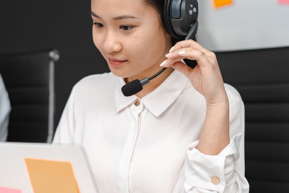 Nhân viên hỗ trợ châu Á làm việc với máy tính và tai nghe